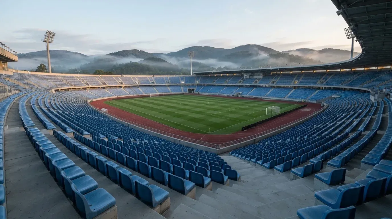 Ein leeres Stadion im Morgenlicht mit Blick auf die Sitzreihen, im Hintergrund Hügel und aufsteigender Nebel.