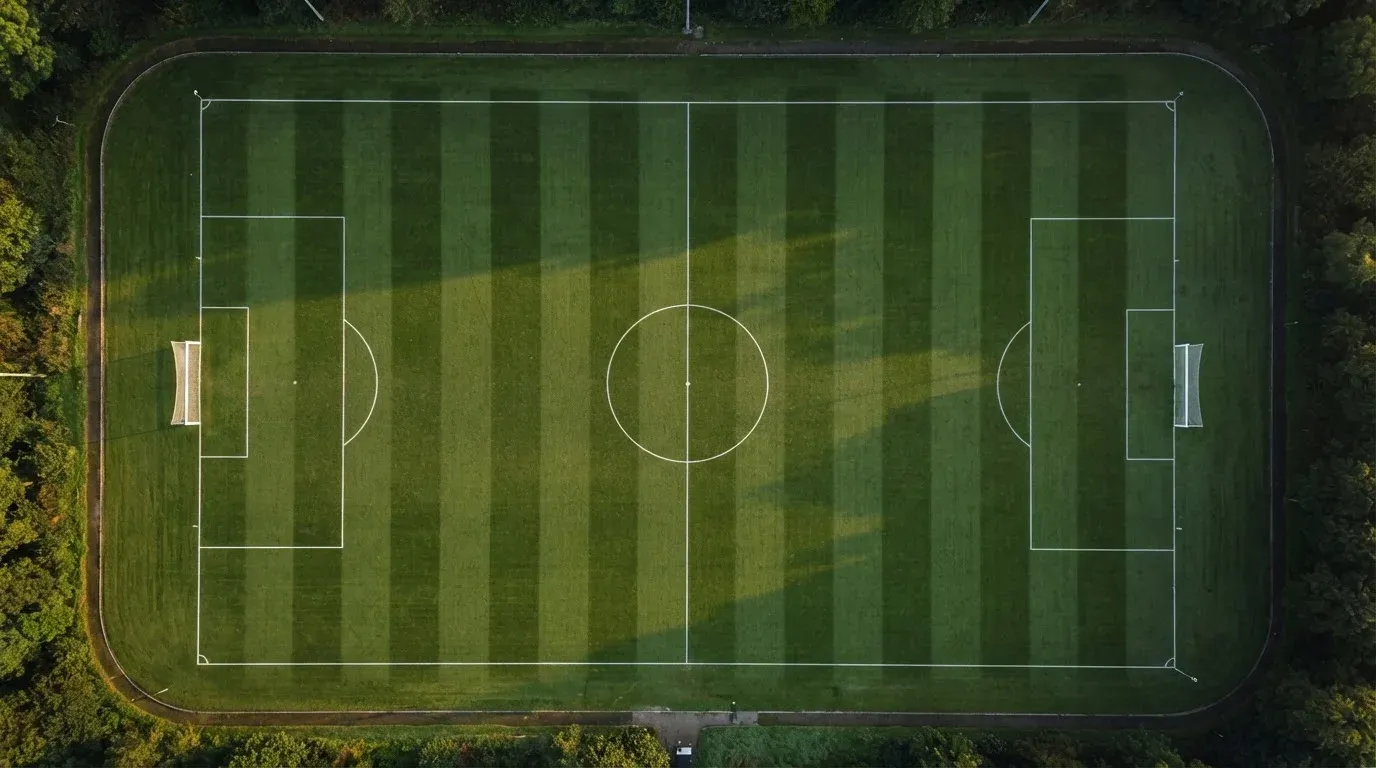 Ein Fussballplatz von oben gesehen, die Linien bilden ein helles Muster auf dem Rasen, Drohnenperspektive in der Morgendämmerung.