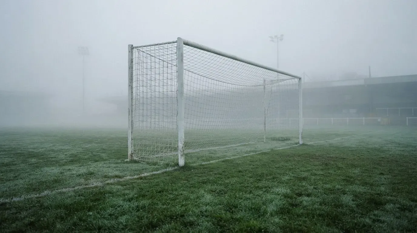 Eine Torlinie mit Netz steht am frühen Morgen im dichten Nebel auf einem Rasenplatz, die Umrisse der Pfosten verschwimmen.