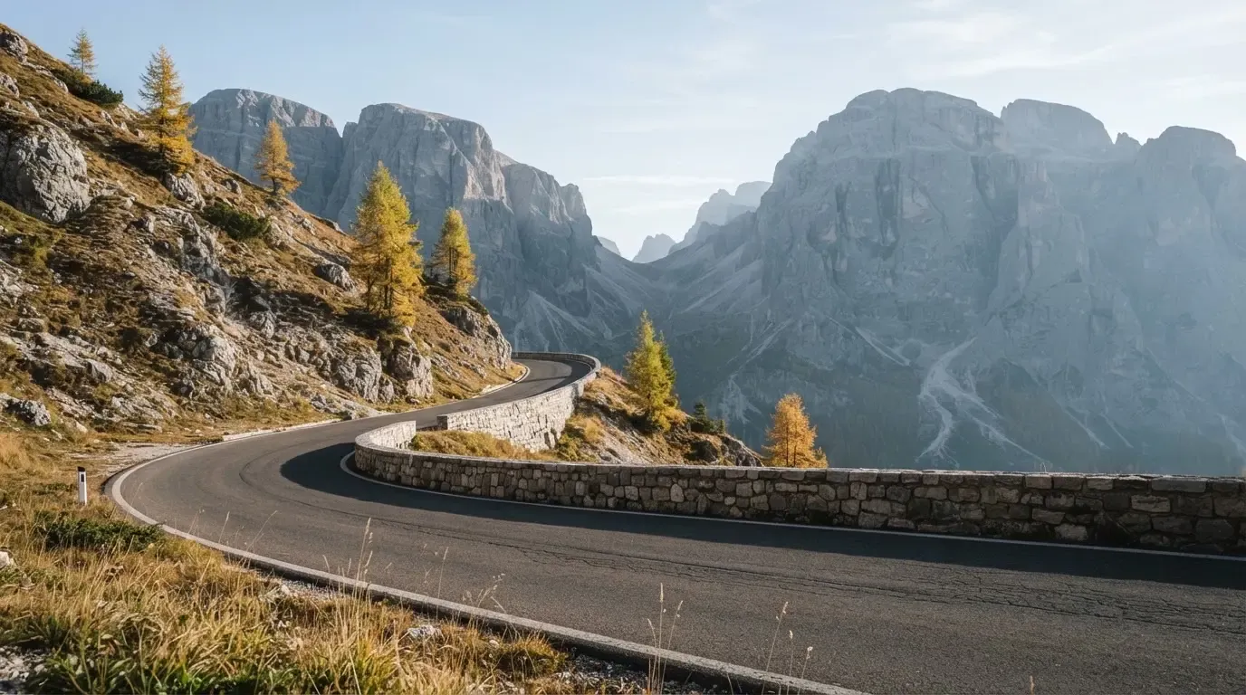 Eine Passstrasse im Hochgebirge säumt eine niedrige Steinmauer, dahinter ragen Felswände auf und der Herbsthimmel ist klar.