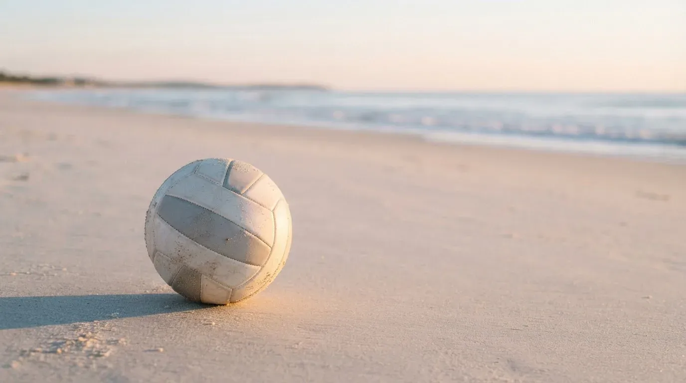 Ein Volleyball liegt auf feinem Sand an einem leeren Strand bei Sonnenaufgang.