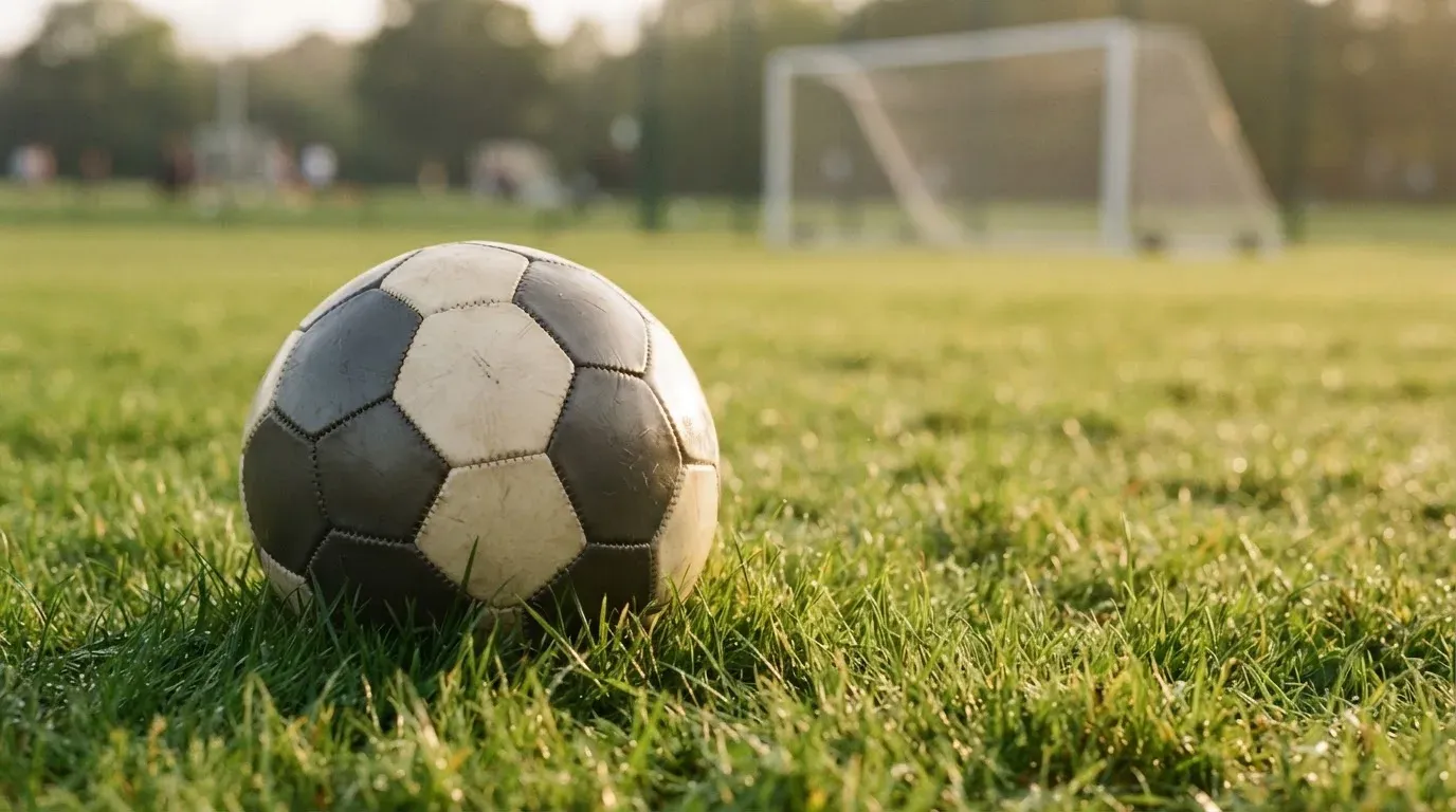 Ein Fussball auf dem Rasen aus niedriger Perspektive aufgenommen, die Torpfosten verschwimmen im Hintergrund.