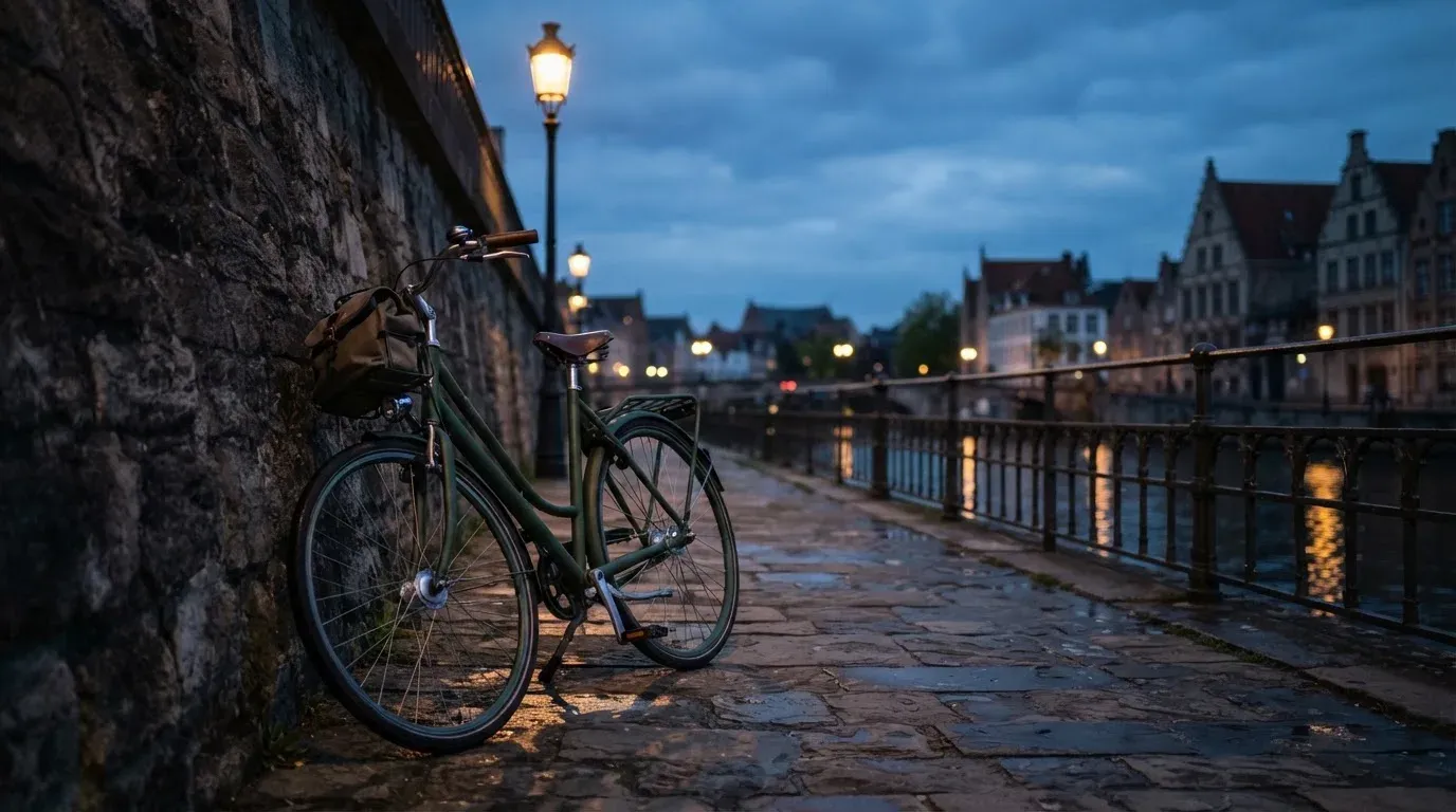 Ein Velo lehnt an einer Steinmauer am Ufer eines Flusses, die Strassenlaternen leuchten in der Dämmerung.