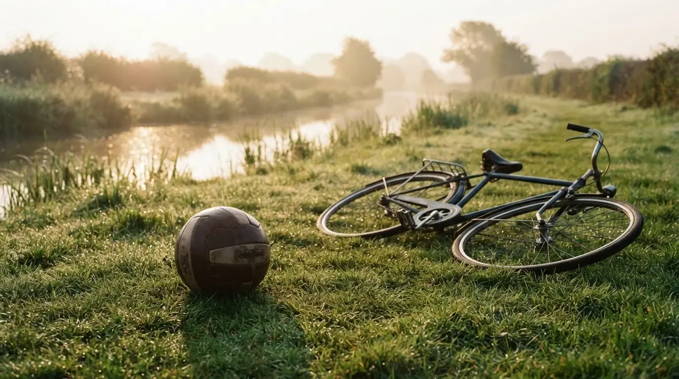 Ein Fussball liegt auf einer Wiese neben einem Fahrrad, im Hintergrund ein Kanal im Morgenlicht