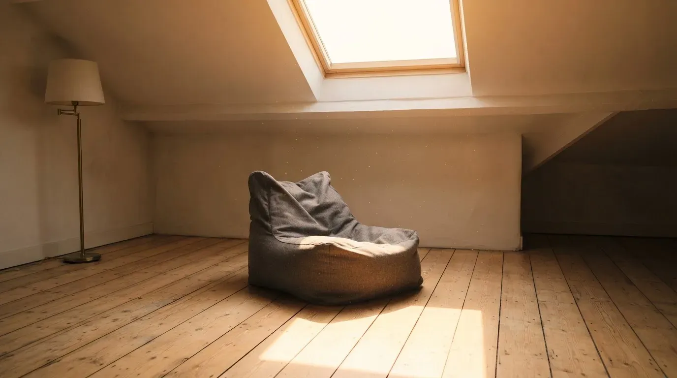 Ein leerer Sitzsack steht in einem Zimmer mit Dachfenster, Abendlicht fällt auf den Holzboden