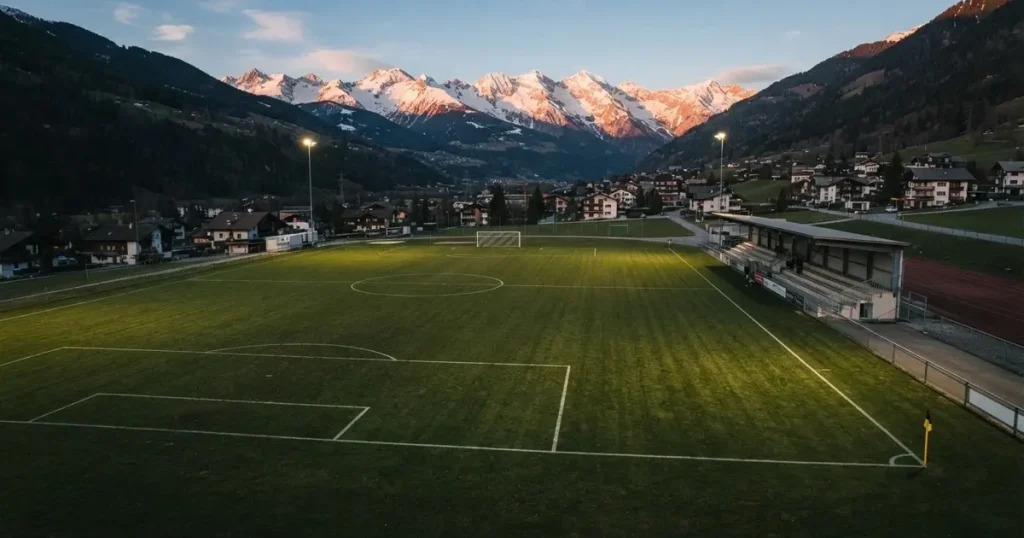 Ein Fussballplatz aus der Vogelperspektive mit sauberen Linien auf dichtem Rasen, in der Ferne verschneite Berge.