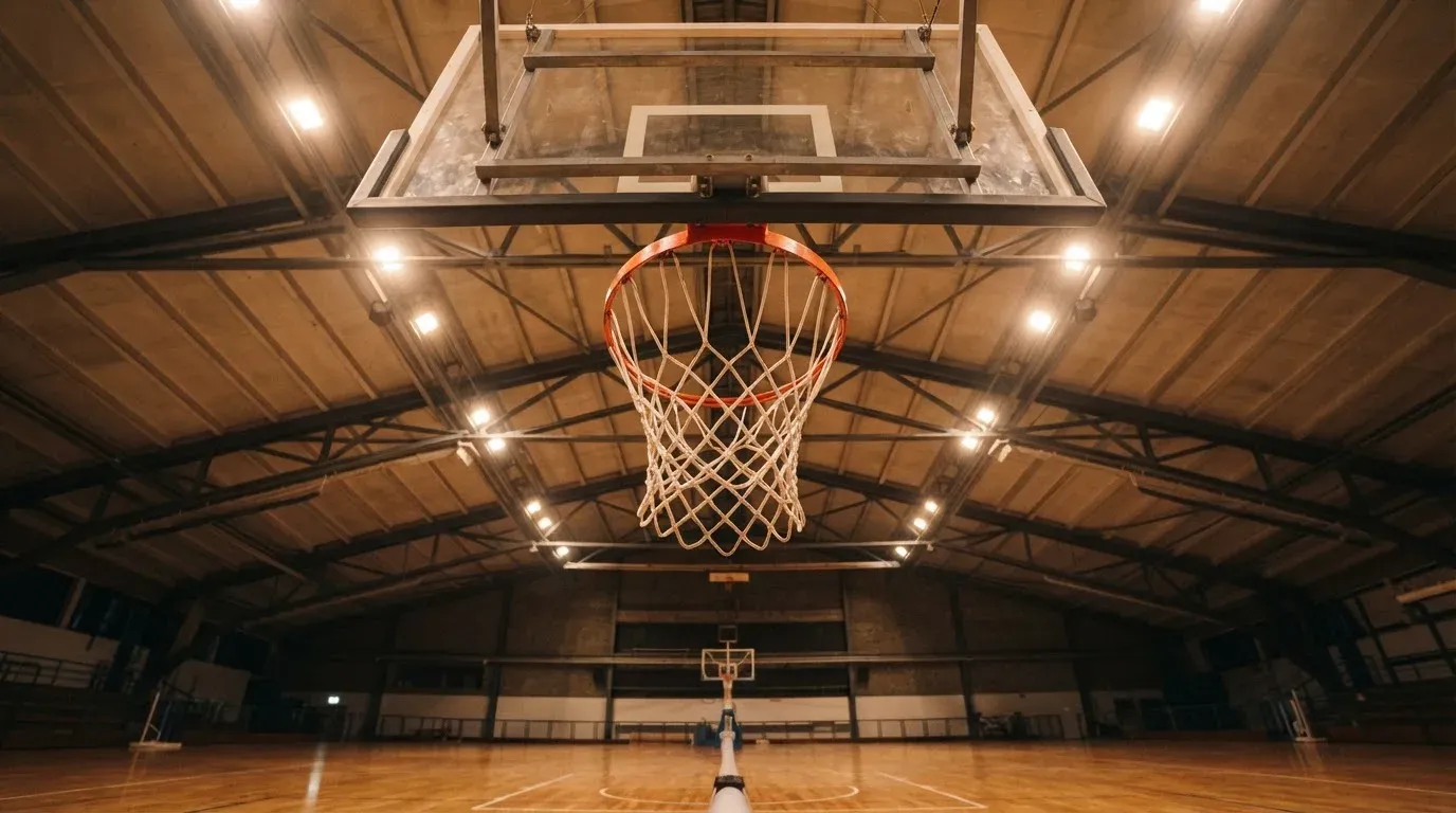Ein Basketballkorb von unten gesehen, darüber eine Hallendecke mit Scheinwerfern und Stahlträgern.