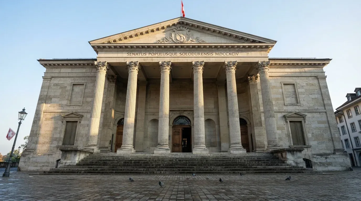 Die Fassade eines Steingebäudes mit Säulen an einem ruhigen Platz im Morgenlicht, ohne Menschen davor.