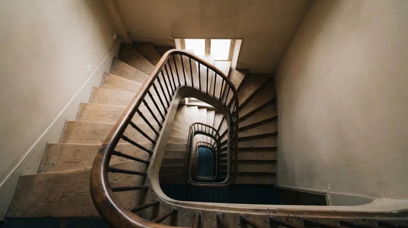 Ein Treppenhaus mit Holzgeländer, von oben fotografiert, die Stufen winden sich nach unten.