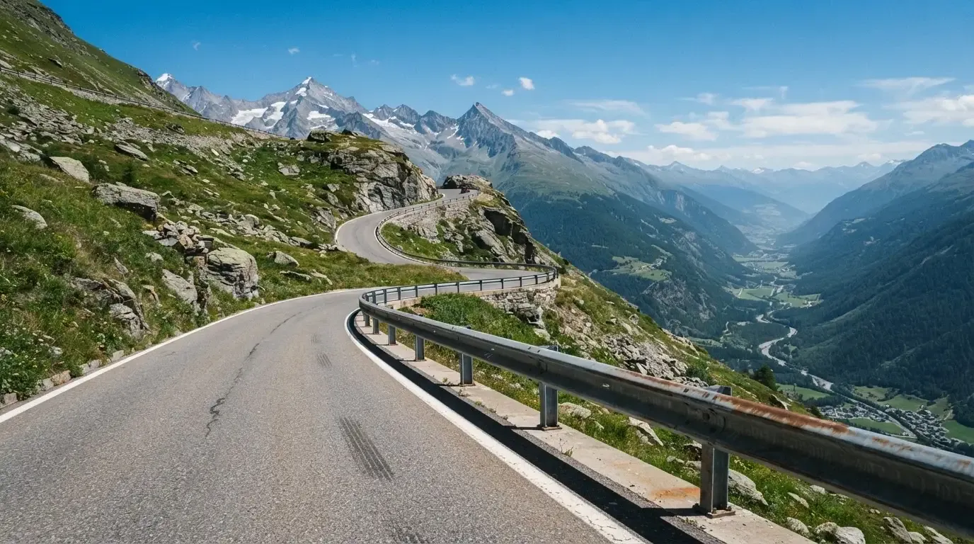 Eine Passstrasse mit Leitplanke windet sich an einem klaren Tag durch eine Berglandschaft.