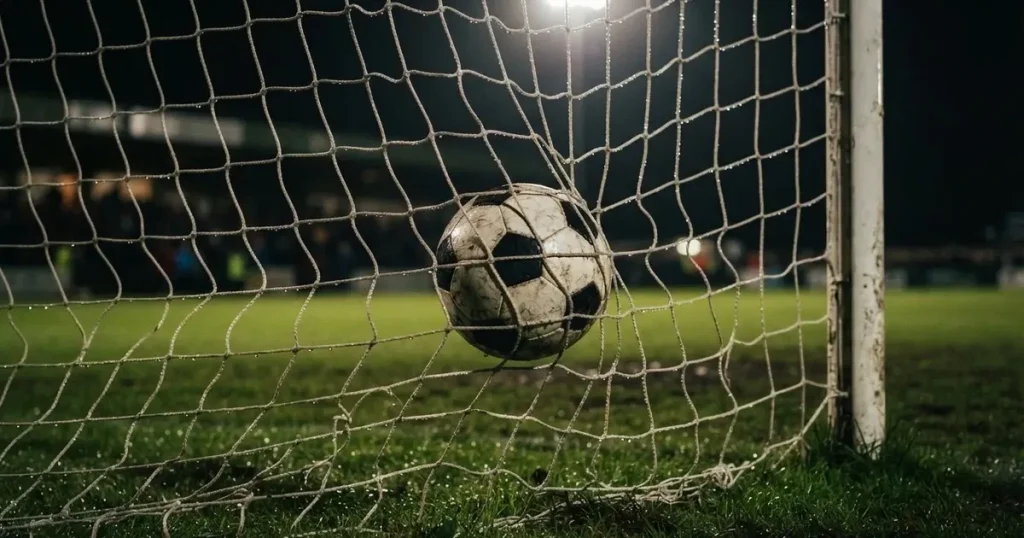 Ein Fussballnetz in Nahaufnahme, in dem ein Ball hängt, Wassertropfen glänzen auf den Maschen.