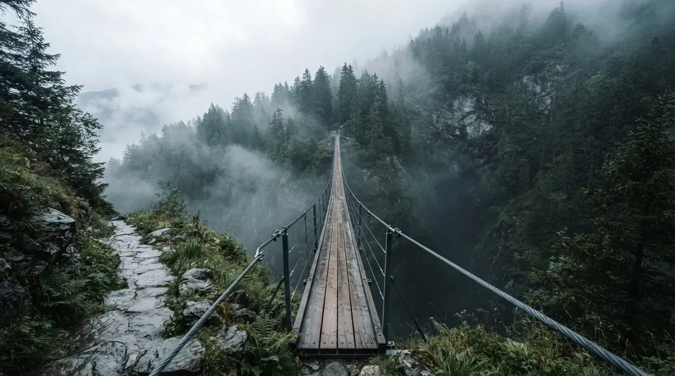 Eine Hängebrücke über eine Schlucht, Nebel steigt auf, dichter Wald bedeckt die steilen Hänge