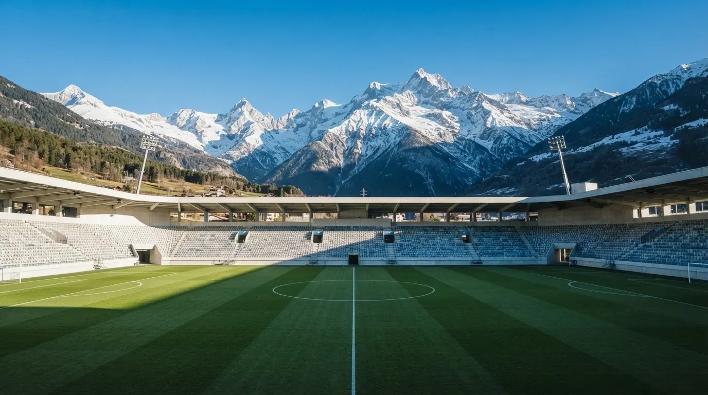 Schneebedeckte Berggipfel erheben sich im klaren Morgenlicht hinter einem leeren Stadion mit hellen Zuschauerrängen.