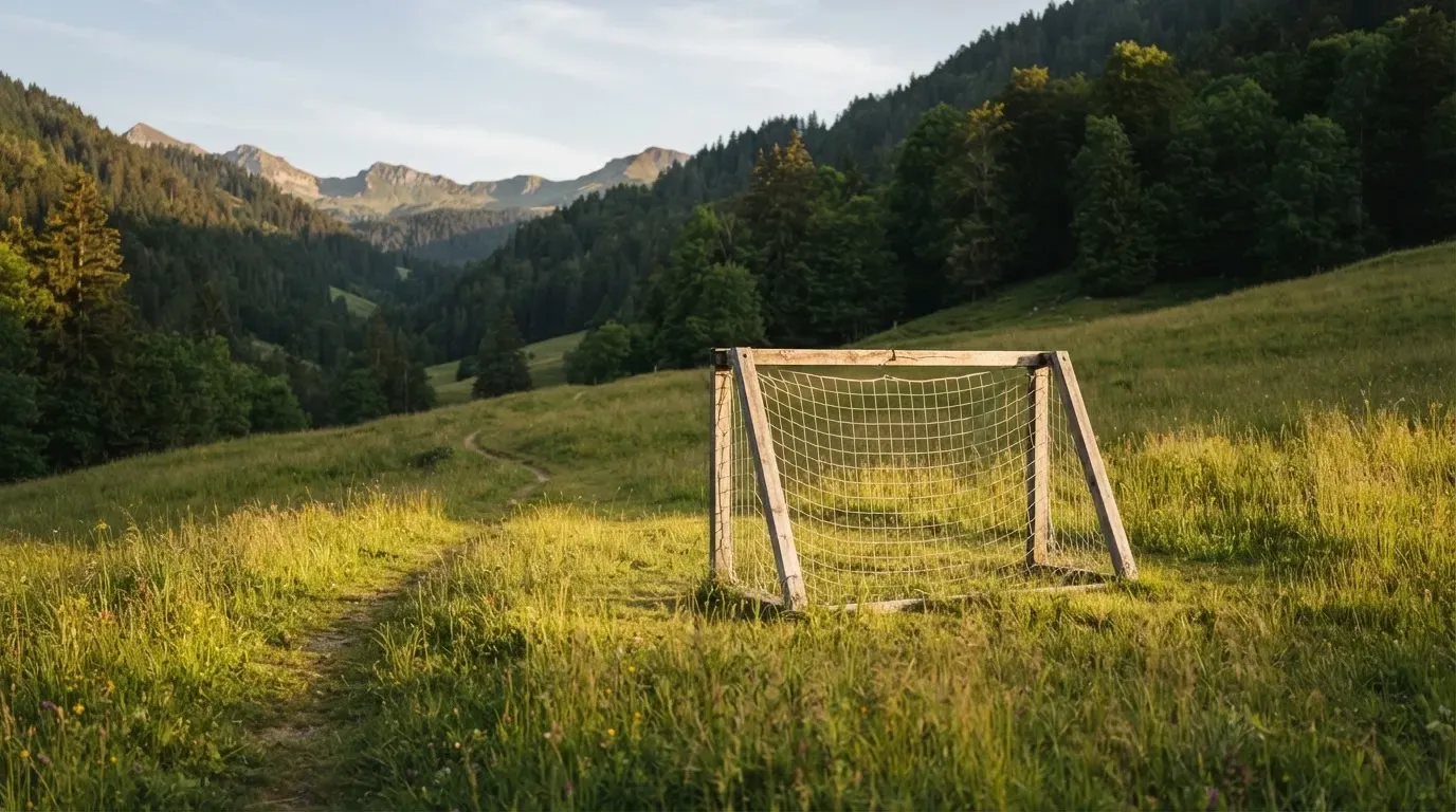 Eine Almwiese mit einem kleinen Holztor für Kinderfussball, dahinter erheben sich bewaldete Hänge im Nachmittagslicht.