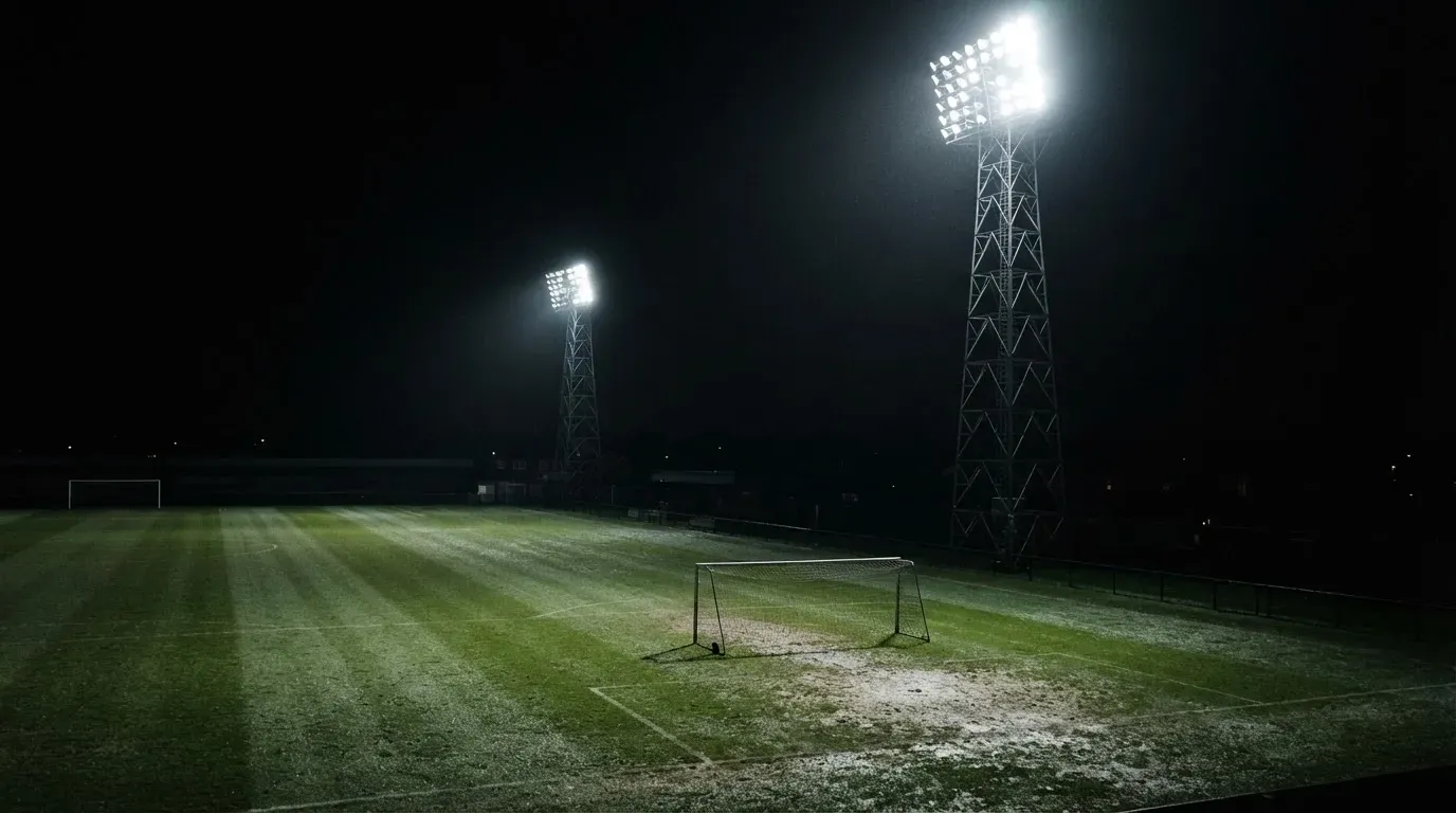 Hohe Flutlichtmasten ragen nachts über einen leeren Trainingsplatz, der Rasen glänzt im weissen Licht.