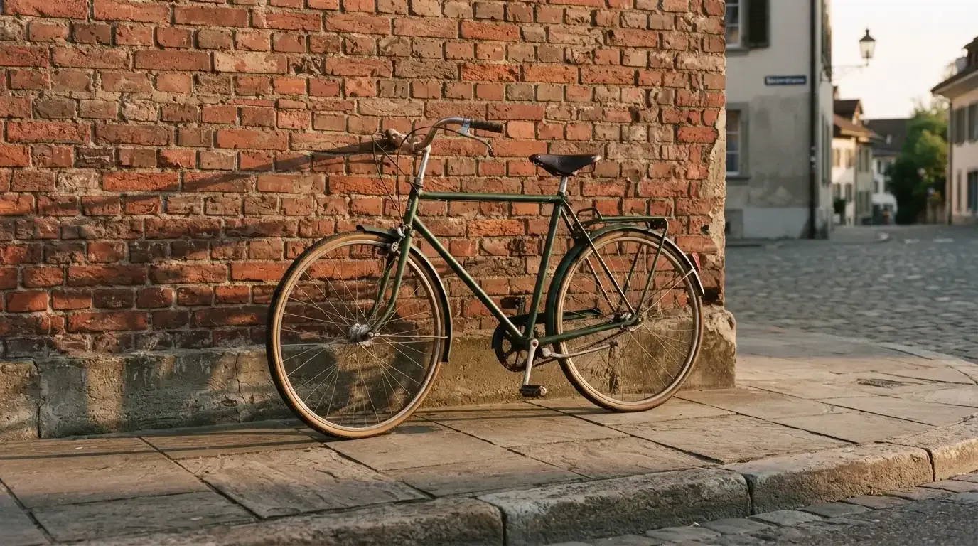 Ein Fahrrad lehnt an einer Backsteinmauer, auf dem Gehweg davor fallen lange Schatten.