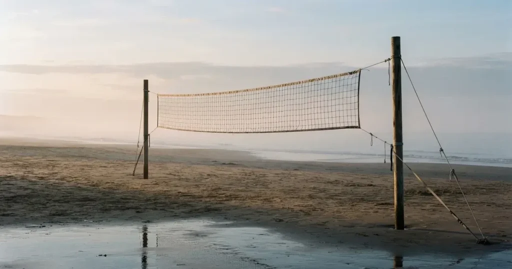 Ein Volleyballnetz spannt sich an einem leeren Sandstrand, das Meer liegt im Dunst.